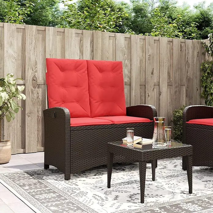 Furnicato Gartenbank PE-Rattan - B x T x H: 105 x 86 x 83 cm, Braun - Braunes Polyrattan-Gartensofa mit roten Kissen und passendem Couchtisch auf einem Outdoor-Teppich.