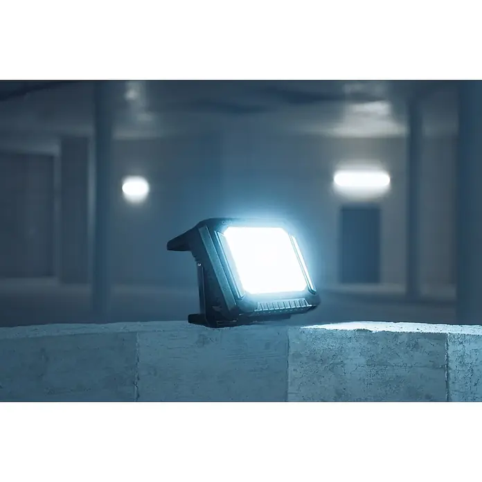 Brennenstuhl Mobiler LED-Strahler Multi Battery Hybridstrahler - L x B x H: 17,7 x 35,4 x 25,8 cm, IP55 - Robuster dunkler Arbeitsstrahler mit heller LED-Anzeige auf einem Betonblock in dunkler Industrieumgebung.