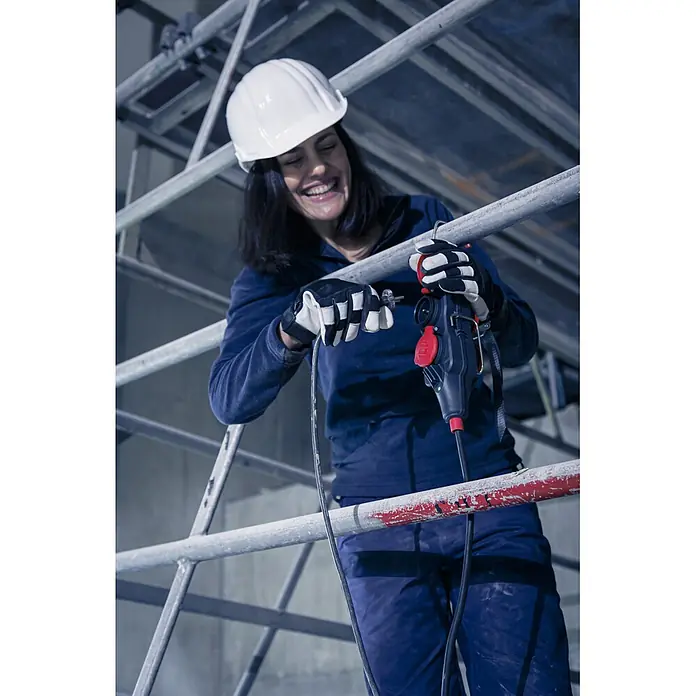 Brennenstuhl Verlängerungskabel mit 4-fach Powerblock - 15 mm, Schwarz, IP44, H07RN-F - Arbeiterin mit Schutzhelm und Handschuhen hält ein schwarz-rotes Elektrowerkzeug mit Kabel auf einem Gerüst.