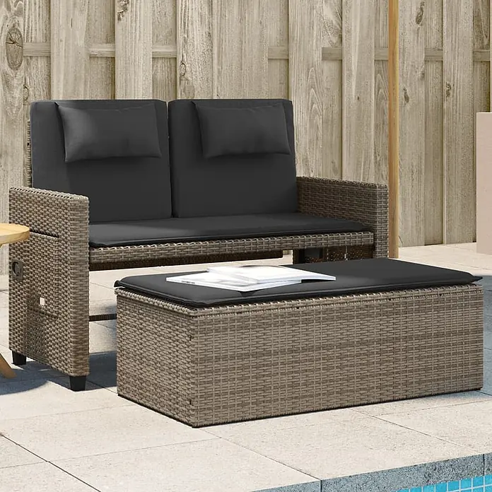 Furnicato Gartenbank PE-Rattan - B x T x H: 122 x 102 x 60 cm, Grau - Braunes Rattan-Gartensofa mit dunkelgrauen Kissen und passendem Ottoman/Couchtisch auf einer Terrasse.