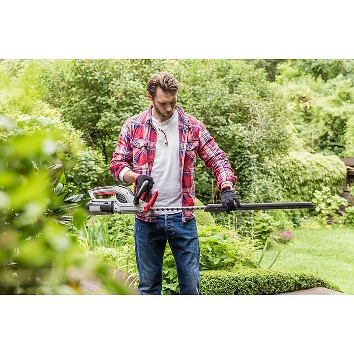 AL-KO 36V Akku-Heckenschere HT 4055 - 36 V, Li-Ionen, Ohne Akku, Schnittlänge: 55 cm - Ein Mann im Garten, der eine Akku-Heckenschere mit grauen und roten Akzenten zum Trimmen der Hecke benutzt.