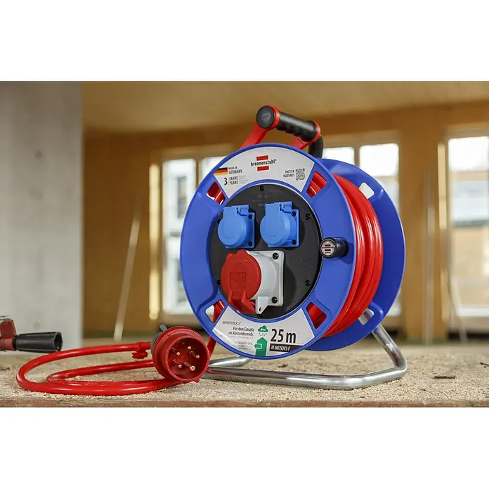 Brennenstuhl Kabeltrommel Garant CEE 1 AT-N07V3V3-G 5G1,5 - Kunststoff, 25 m, IP44 - Robuste rot-blaue Kabeltrommel mit mehreren Steckdosen, darunter CEE und Standard, auf Holzboden in einer Werkstatt.