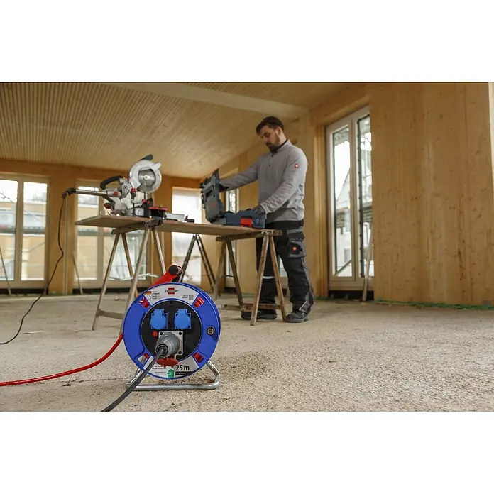 Brennenstuhl Kabeltrommel Garant CEE 1 AT-N07V3V3-G 5G1,5 - Kunststoff, 25 m, IP44 - Blaue und rote Kabeltrommel versorgt Werkzeuge auf einer Baustelle, mit einem Arbeiter im Hintergrund.