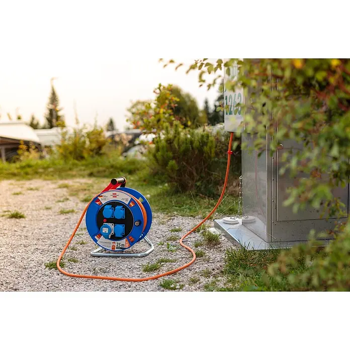 Brennenstuhl Kabeltrommel Garant CEE IP44 Camping H07RB-F 3G2,5 - Kunststoff, 25 m, IP44 - Blaue Brennenstuhl Kabeltrommel mit orangefarbenem Kabel und blauen Steckdosen, angeschlossen an eine Stromversorgung auf einem Campingplatz.