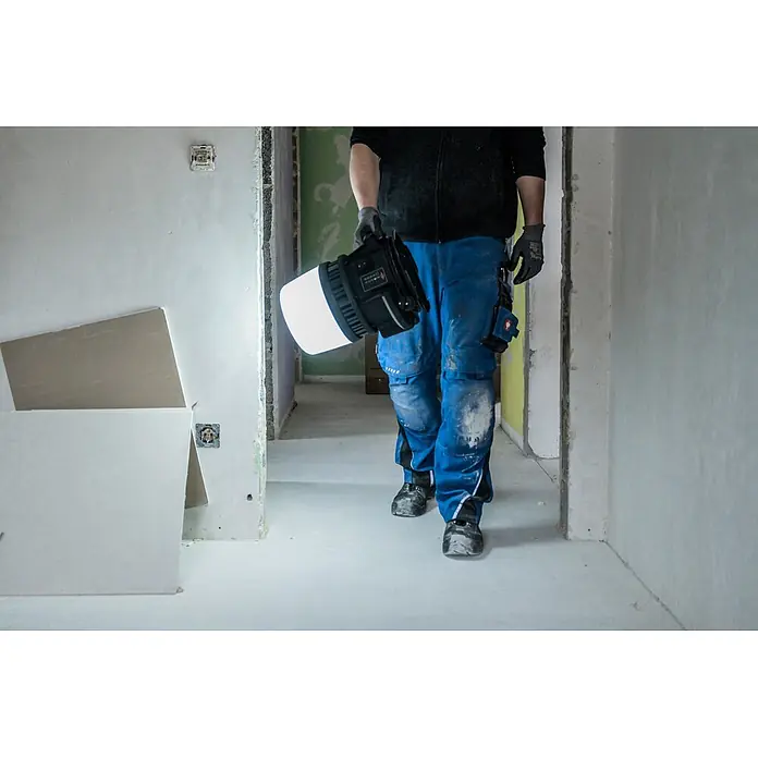 Brennenstuhl Mobiler LED-Strahler Multi Battery Hybrid - L x B x H: 28,6 x 28 x 37,8 cm, IP54 - Robuste schwarz-weiße LED-Arbeitsleuchte, von Arbeiter auf Baustelle getragen.