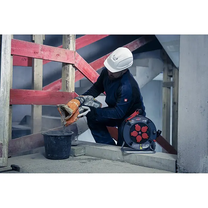 Brennenstuhl Kabeltrommel 300 KU 2200 - Kunststoff, 25 m, H07RN-F, IP44 - Schwarze und rote brennenstuhl® 25m Kabeltrommel mit Mehrfachsteckdosen auf einer Baustelle für den robusten Einsatz.