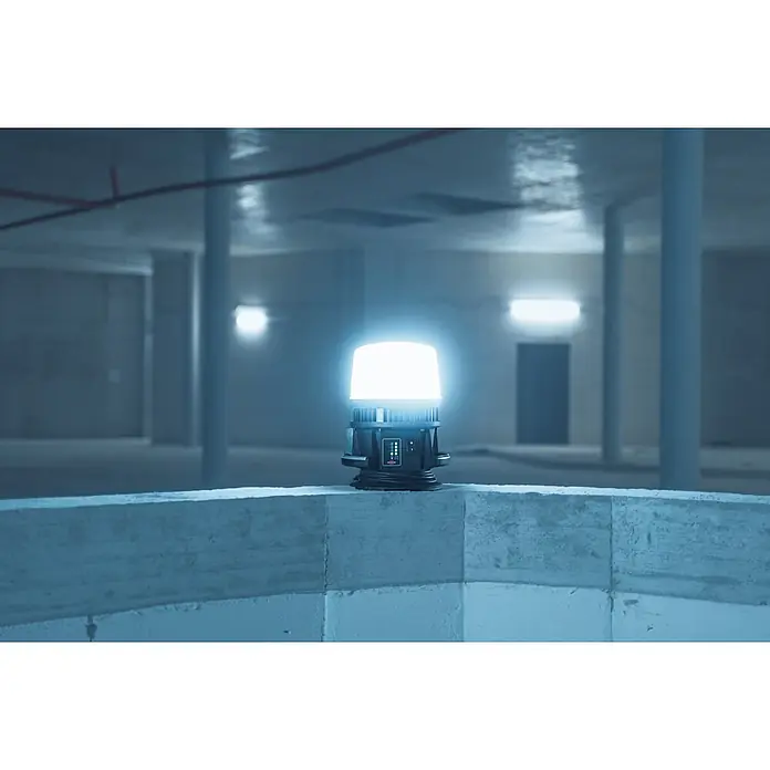 Brennenstuhl Mobiler LED-Strahler Multi Battery Hybrid - L x B x H: 28,6 x 28 x 37,8 cm, IP54 - Helle, weiße, tragbare Arbeitsleuchte mit dunklem Gehäuse auf einem Betonvorsprung, beleuchtet einen dämmrigen Betonraum.