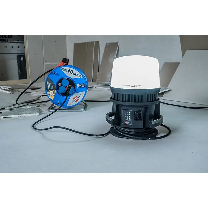Brennenstuhl Mobiler LED-Strahler Multi Battery Hybrid - L x B x H: 28,6 x 28 x 37,8 cm, IP54 - Eine blaue 40m Kabeltrommel und eine weiß-schwarze Multi-Akku Arbeitsleuchte auf Betonboden auf einer Baustelle.