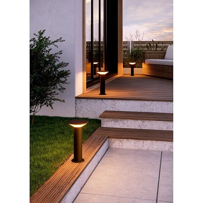 Eglo Rigosa Sobremuro exterior - 10 W - Balizas negras iluminando un espacio exterior moderno con tarima de madera, escaleras y césped, creando un ambiente cálido.