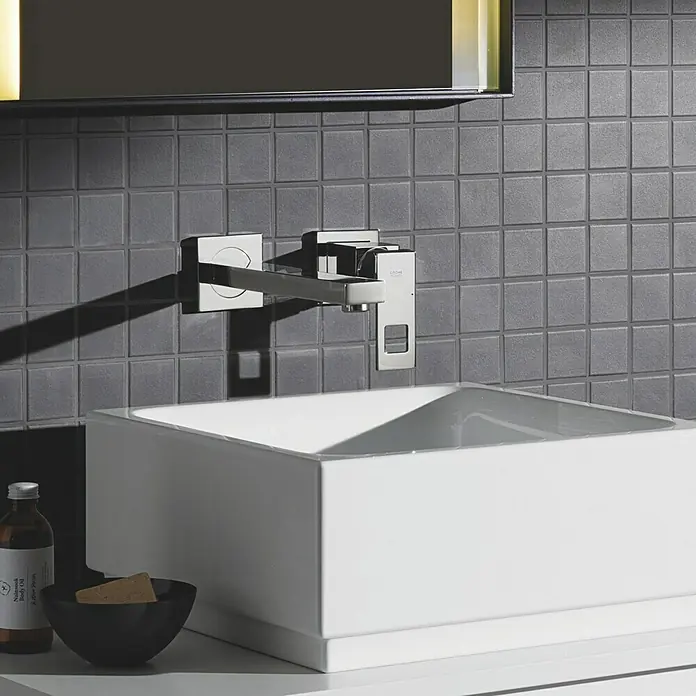 Grohe Eurocube Waschtischarmatur - Wandmontage, Chrom, Glänzend, Ausladung Armatur: 231 mm - Elegantes Badezimmerdesign mit einem modernen, wandmontierten Wasserhahn über einem quadratischen Waschbecken, akzentuiert durch graue Fliesen und dezente Beleuchtung.