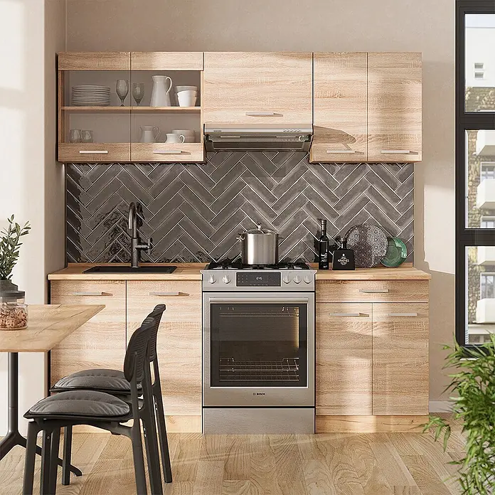 Vicco Küchenzeile R-Line Sonoma/Goldkraft Eiche ohne Arbeitsplatte - Sonoma, Ohne Elektrogeräte - Eine moderne Küche aus hellem Holzmaserung mit dunkelgrauer Fischgrät-Rückwand, Edelstahlgeräten und schwarzer Spüle.
