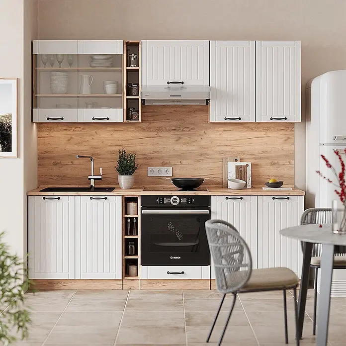 Vicco Küchenzeile Fame-Line Weiß Landhaus, AP Marmor - Weiß Landhaus, Ohne Elektrogeräte - Weiße vertäfelte Küchenschränke mit Holztheke & Spritzschutz, Einbaugeräten und schwarzen Griffen in einer hellen Küche.