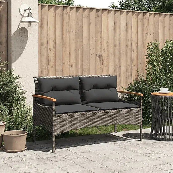 Furnicato Gartenbank PE-Rattan - B x T x H: 116 x 62,5 x 74 cm, Grau - Grau geflochtenes Rattan-Zweisitzer-Gartensofa mit dunkelgrauen Kissen und Holzarmlehnen auf einer Terrasse.