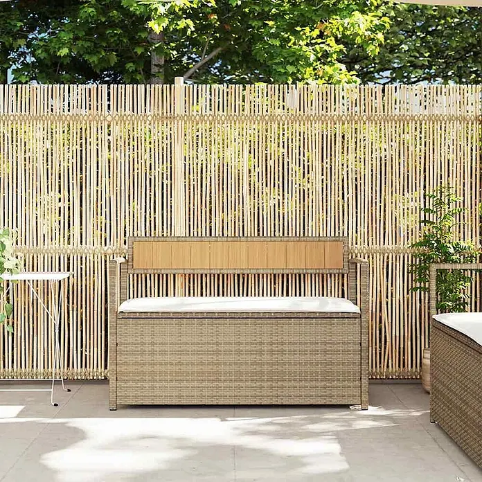 Furnicato Gartenbank - B x T x H: 111,5 x 54 x 74 cm, Beige und Cremeweiß - Beige Rattan-Gartenbank mit Stauraum, Holzrückenlehne und weißem Kissen, in einem Garten mit Bambuszaun.