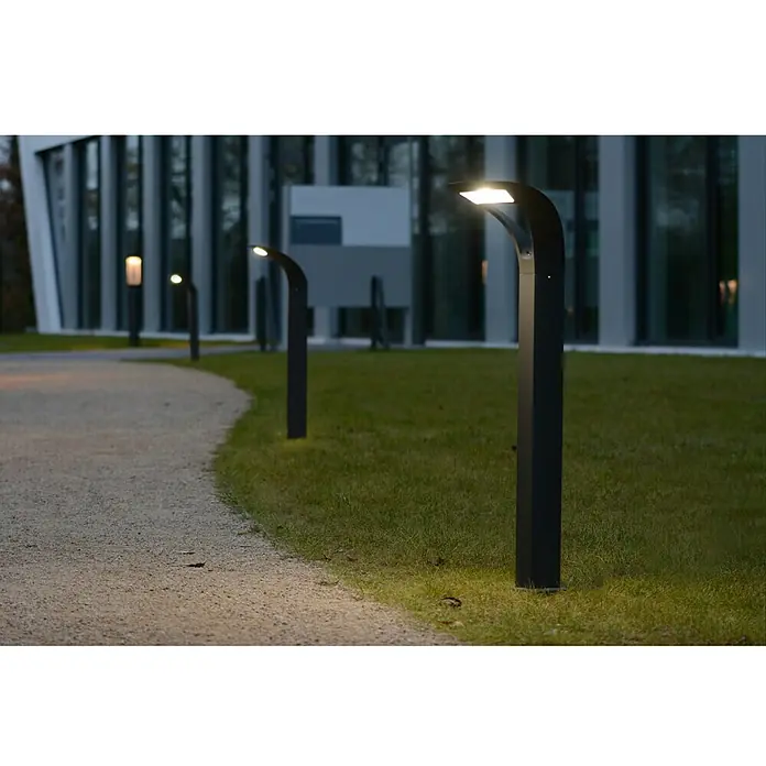 Lutec Sobremuro exterior Anda - 18 W, Blanco neutro, 26,4 x 26,4 x 80 cm, Con bombillas - Luces de jardín modernas bordean un camino, iluminando un edificio. El diseño elegante se integra perfectamente en el paisaje.