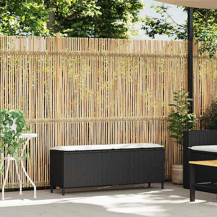 Furnicato Gartenbank PE-Rattan - B x T x H: 110 x 30 x 40,5 cm, Schwarz und Creme - Schwarze Rattan-Gartenaufbewahrungsbox mit weißem Kissen auf einer Terrasse vor einem Bambuszaun.