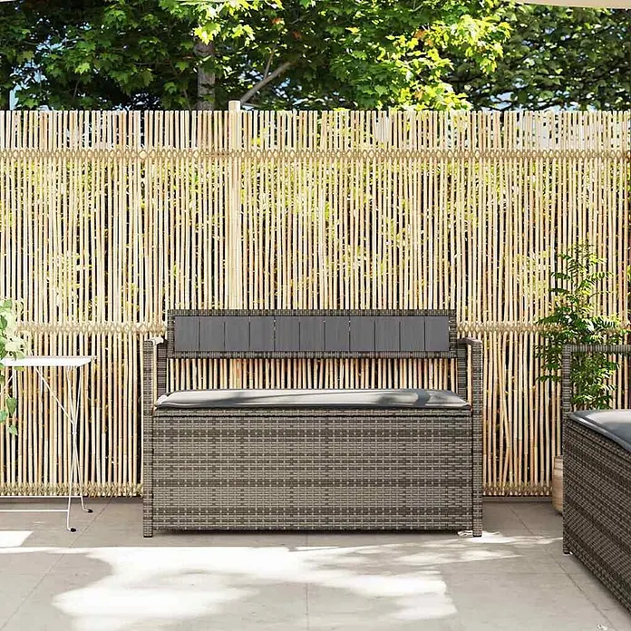 Furnicato Gartenbank PE-Rattan - B x T x H: 111,5 x 54 x 74 cm, Grau und Dunkelgrau - Graue Outdoor-Aufbewahrungsbank aus Korbgeflecht mit Kissen auf einer Terrasse vor einem Bambuszaun.