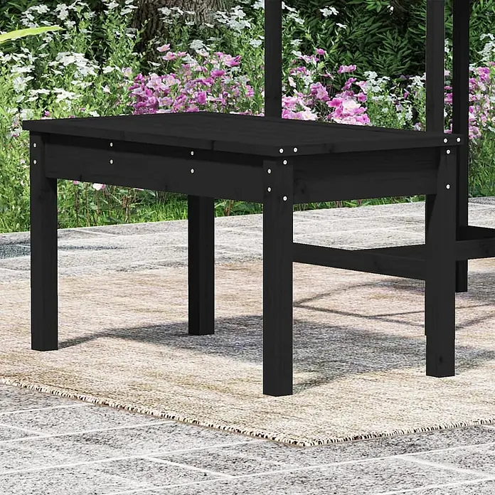 Furnicato Gartenbank Kiefer-Massivholz - B x T x H: 80 x 44 x 45 cm, Schwarze Kiefer - Schwarzer Gartentisch aus Holz auf einem Terrassenteppich, umgeben von grünen Pflanzen und rosa Blumen.