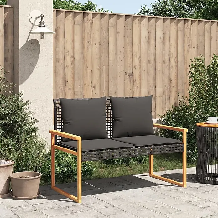 Furnicato Gartenbank - B x T x H: 61 x 119 x 79 cm, Schwarz - Zweisitzer-Gartenbank mit dunkelgrauen Kissen, dunklem Flechtsitz und hellem Holzrahmen auf einer gepflasterten Terrasse.