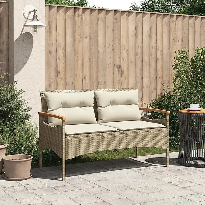 Furnicato Gartenbank PE-Rattan - B x T x H: 116 x 62,5 x 74 cm, Beige - Beiges Rattan-Optik 2-Sitzer Gartensofa mit cremefarbenen Kissen und Holzarmlehnen auf einer Terrasse.