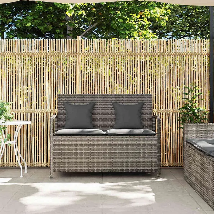 Furnicato Gartenbank - B x T x H: 111 x 56 x 87 cm, Grau und Dunkelgrau - Graue Rattan-Sitzbank mit Stauraum und dunklen Kissen, auf einer Terrasse vor einem Bambuszaun.