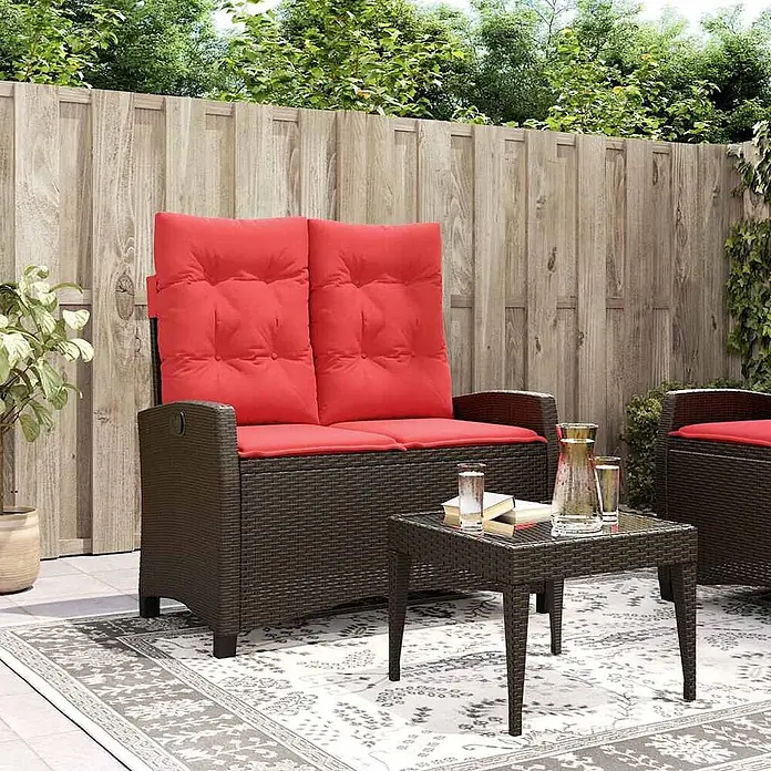 Furnicato Gartenbank - B x T x H: 105 x 90 x 93 cm, Braun - Dunkelbraunes Polyrattan-Gartenmöbelset mit roten Kissen, bestehend aus Zweiersofa und Couchtisch, auf einer Terrasse.