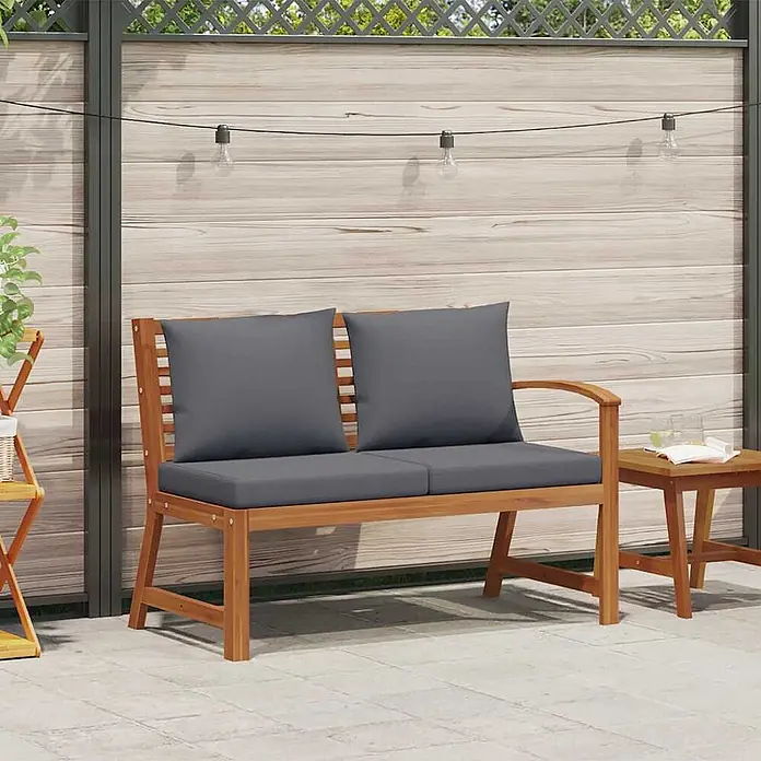 Furnicato Gartenbank Akazienholz geölt - B x T x H: 114,5 x 60,5 x 81 cm, Dunkelgrau - Hölzerne 2-Sitzer Gartenbank mit dunkelgrauen Kissen, auf einer Terrasse neben einem kleinen Holztisch.