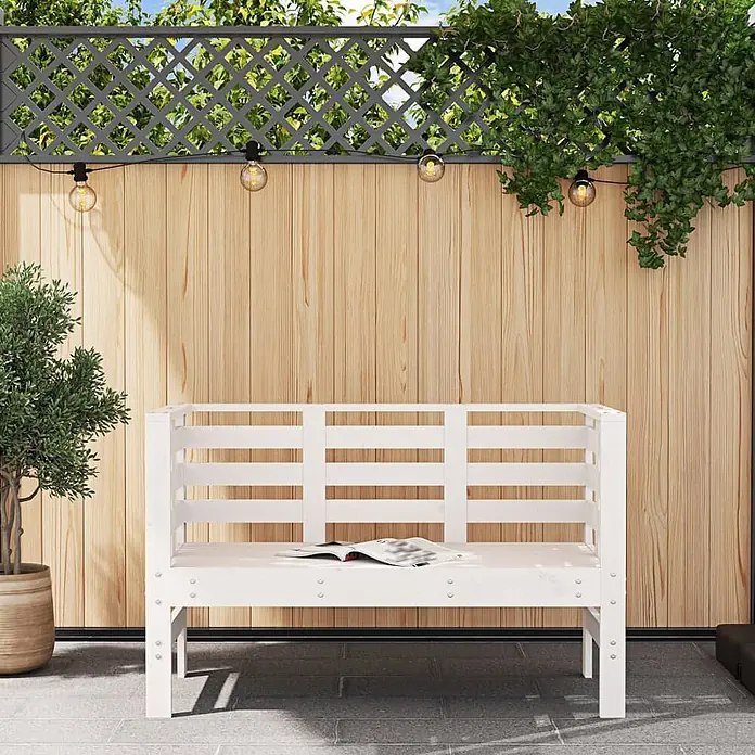 Furnicato Gartenbank Kiefernholz-Massivholz - B x T x H: 111,5 x 53 x 71 cm, Weiße Kiefer - Weiße Holzbank für den Außenbereich mit Zeitschrift, vor einem Holzzaun mit Pflanzen.