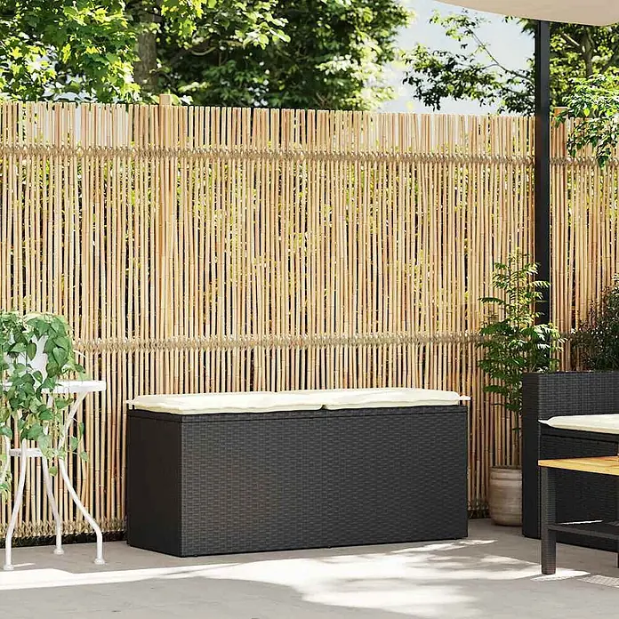Furnicato Gartenbank - B x T x H: 110 x 40 x 44 cm, Schwarz - Dunkelgraue Outdoor-Aufbewahrungsbox in Rattan-Optik mit zwei cremefarbenen Kissen auf einer Terrasse.