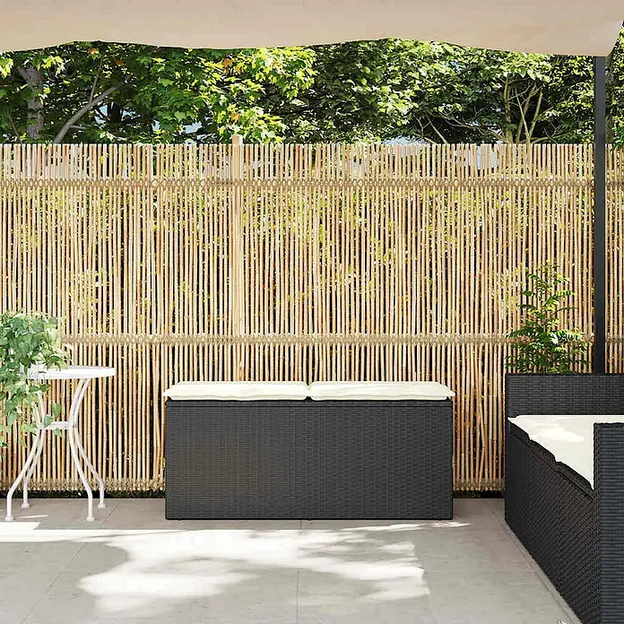 Furnicato Gartenbank PE-Rattan - B x T x H: 110 x 40 x 44 cm, Schwarz - Natürlicher Bambus-Sichtschutzzaun für die Terrasse, mit einer dunkelgrauen Rattan-Sitzbox und einem Sofa mit hellen Kissen.