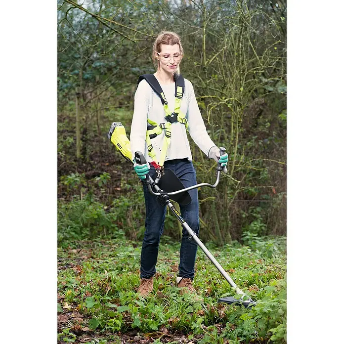 Ryobi ONE+ Akku-Rasentrimmer RBC 18X20B4F - 18 V, 4 Ah, Li-Ionen, 1 Akku, Schnittbreite Messer: 20 cm, Schnittbreite Faden: 30 cm - Eine Frau, die eine Ryobi Akku-Sense mit Tragegurt benutzt, trägt Schutzkleidung und arbeitet im Garten.