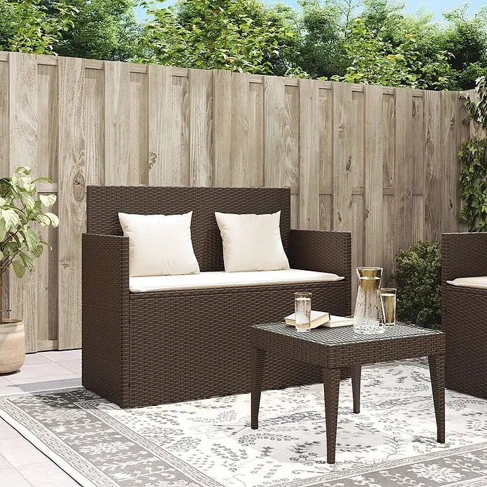Furnicato Gartenbank PE-Rattan - B x T x H: 120 x 50 x 90,5 cm, Braun - Dunkelbraunes Rattan-Gartensofa und Tisch mit cremefarbenen Kissen auf einem Outdoorteppich.