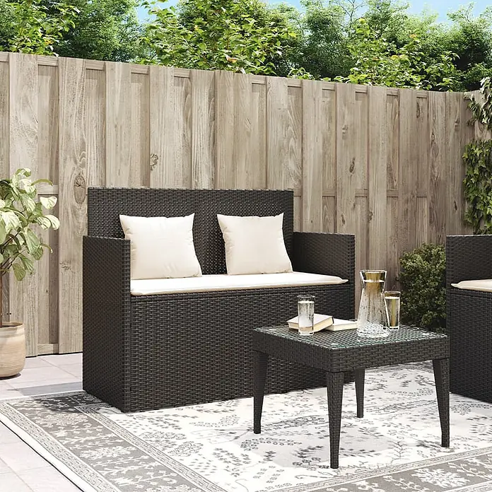 Furnicato Gartenbank PE-Rattan - B x T x H: 120 x 50 x 90,5 cm, Schwarz und Creme - Dunkelbraunes Rattan-Gartenmöbelset mit cremefarbenen Kissen, bestehend aus Zweiersofa und Tisch, auf einem gemusterten Teppich.