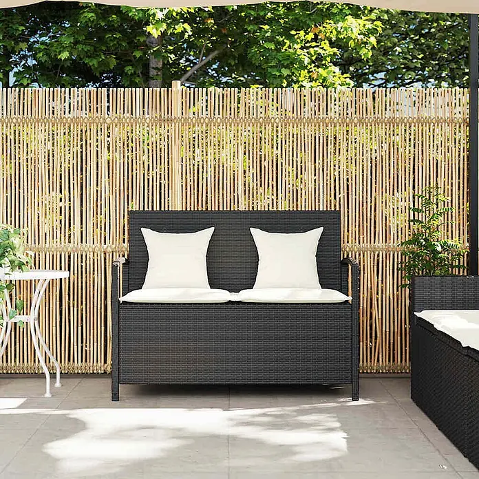Furnicato Gartenbank PE-Rattan - B x T x H: 111 x 56 x 87 cm, Schwarz und Creme - Dunkelgraue Rattan-Gartenbank mit weißen Kissen auf einer Terrasse vor einem Bambuszaun.
