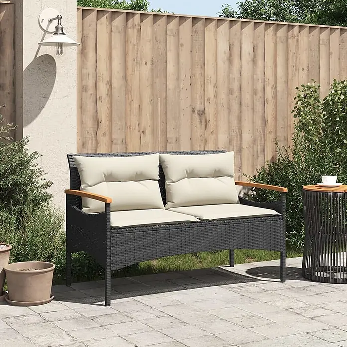 Furnicato Gartenbank PE-Rattan - B x T x H: 116 x 62,5 x 74 cm, Schwarz - Schwarzes Rattan 2-Sitzer Outdoor-Sofa mit cremefarbenen Kissen und Holzarmlehnen auf einer Terrasse.