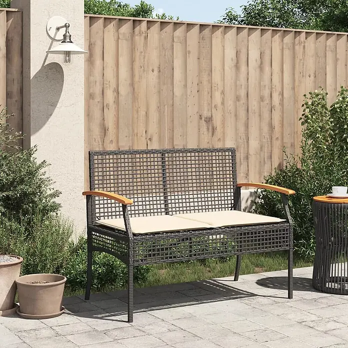 Furnicato Gartenbank PE-Rattan - B x T x H: 108 x 57 x 85 cm, Schwarz - Dunkelgraue Rattan-Gartenbank mit hellen Holzarmlehnen und beigen Kissen auf einer Terrasse, neben einem passenden Beistelltisch.