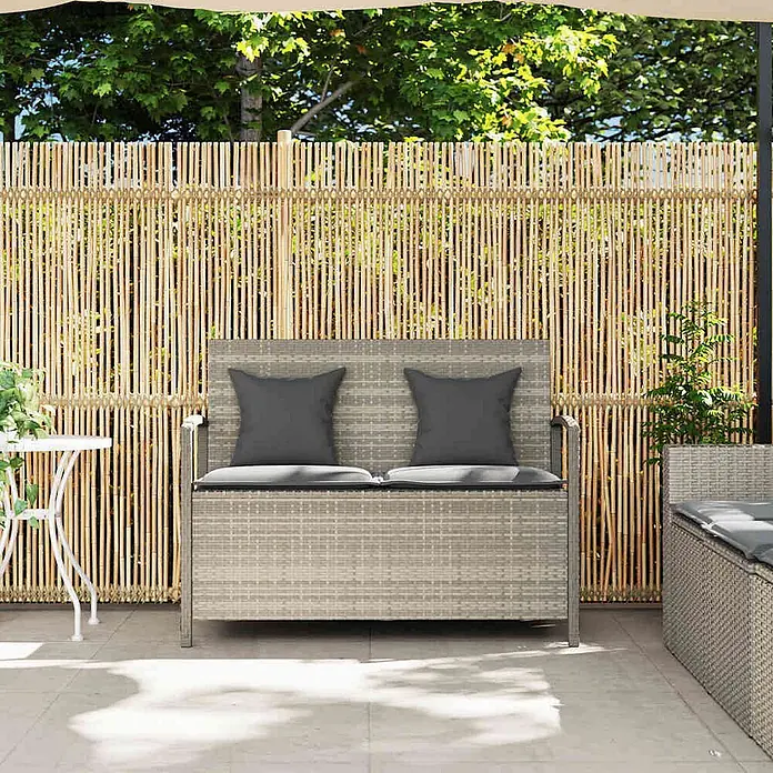 Furnicato Gartenbank PE-Rattan - B x T x H: 111 x 56 x 87 cm, Hellgrau und Dunkelgrau - Graue Rattan-Sitzbank mit Stauraum und zwei dunkelgrauen Kissen auf einer Terrasse vor einem Bambuszaun.