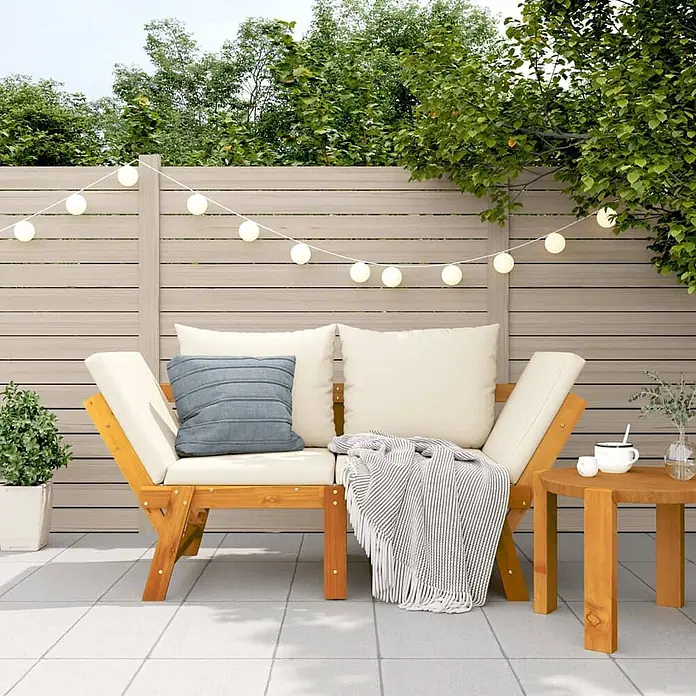 Furnicato Gartenbank Akazien-Massivholz geölt - B x T x H: 205 x 74 x 66 cm, Cremeweiß - Hölzerne Gartenbank mit cremefarbenen Kissen, blauem Kissen, gestreifter Decke und rundem Beistelltisch auf einer Terrasse.