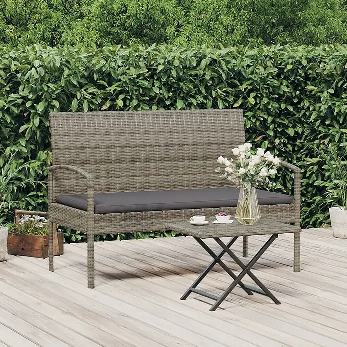 Furnicato Gartenbank - Grau - Graue Outdoor-Sitzbank im Rattan-Stil mit dunklem Kissen und passendem kleinen Klapptisch auf einer Holzterrasse.
