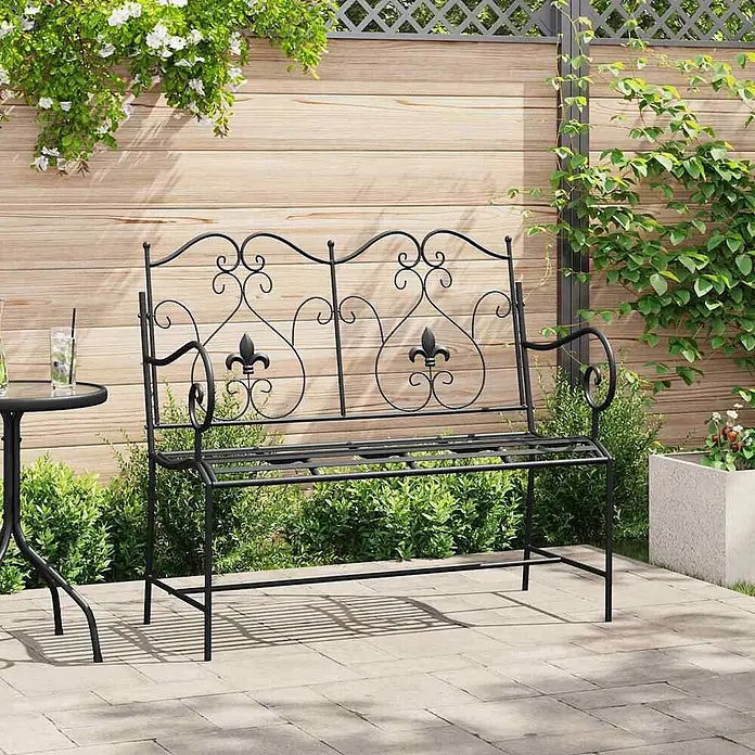 Furnicato Gartenbank Stahl - B x T x H: 54 x 104 x 93 cm, Schwarz - Schwarze Metallgartenbank mit dekorativer Rückenlehne und zwei Fleur-de-lis-Motiven auf einer Terrasse.