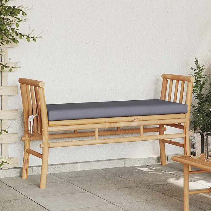 Furnicato Gartenbank Bambus - B x T x H: 38 x 110 x 65 cm, Dunkelgrau - Bambus-Gartenbank mit grauem Kissen auf einer Terrasse mit Pflanzen.