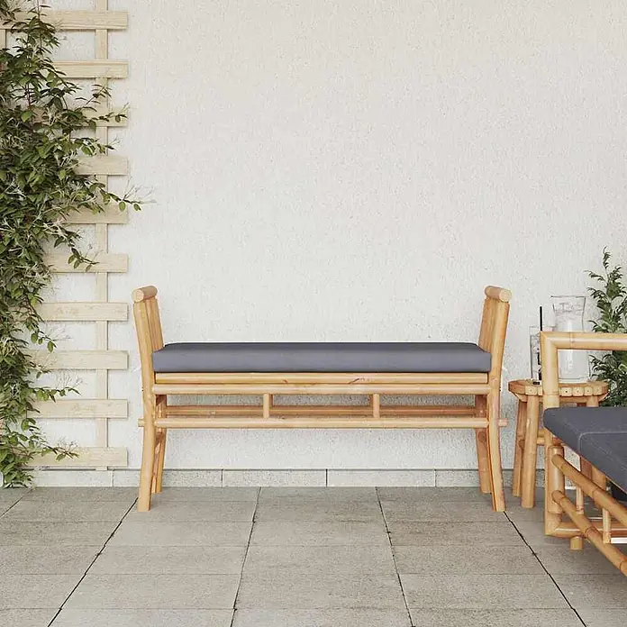Furnicato Gartenbank Bambus - B x T x H: 38 x 110 x 65 cm, Dunkelgrau - Outdoor-Bambusbank mit grauem Kissen auf einer Terrasse, neben einem passenden Beistelltisch.