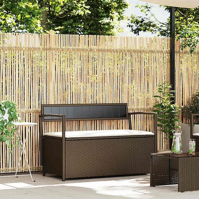 Furnicato Gartenbank PE-Rattan - B x T x H: 111,5 x 54 x 74 cm, Braun und Cremeweiß - Dunkelbraune Rattan-Gartenbank mit Stauraum, weißem Kissen und schwarzer Rückenlehne auf einer Terrasse.