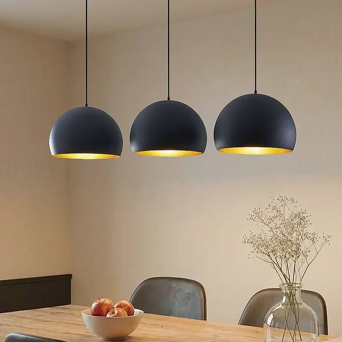 Lindby Pendelleuchte Tarjei - L x B x H: 146 x 40 x 28 cm, schwarz, Schwarz, gold, E27 - Drei matte schwarze Pendelleuchten mit goldfarbenen Innenseiten beleuchten einen Esstisch.