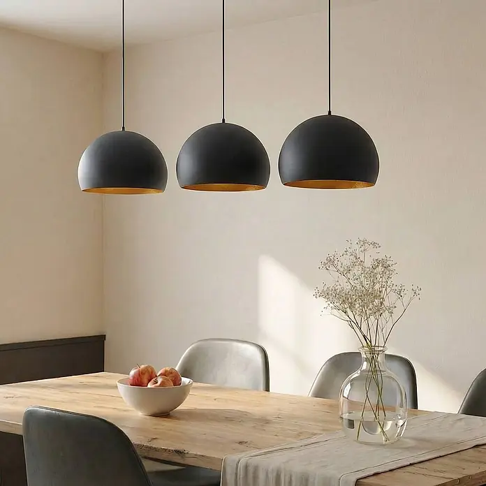 Lindby Pendelleuchte Tarjei - L x B x H: 146 x 40 x 28 cm, schwarz, Schwarz, gold, E27 - Drei schwarze Pendelleuchten mit goldener Innenseite hängen über einem Holzesstisch.