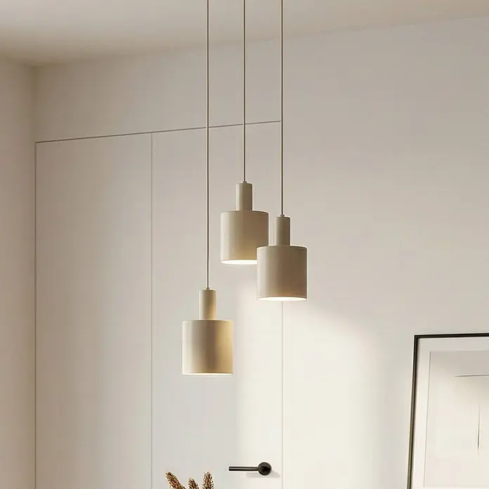 Lindby Pendelleuchte Ovelia - L x B x H: 43 x 43 x 150 cm, creme / amber, beige, E27 - Drei cremefarbene zylindrische Pendelleuchten hängen in unterschiedlichen Höhen in einem minimalistischen Raum.