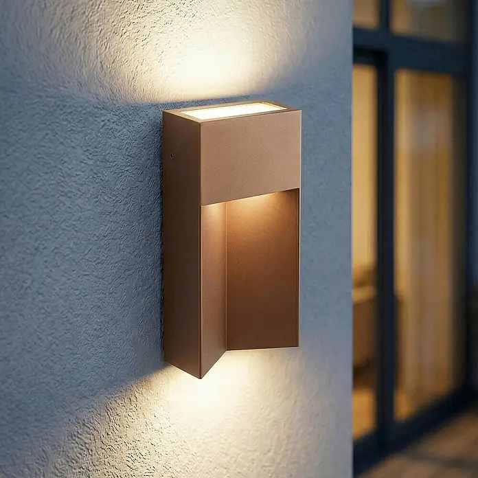 Lucande Außenwandleuchte Kaholo - braun / rost, braun / rost, IP44 - Rechteckige bronzene Außenwandleuchte wirft warmes Auf- und Ablicht auf eine strukturierte Wand.
