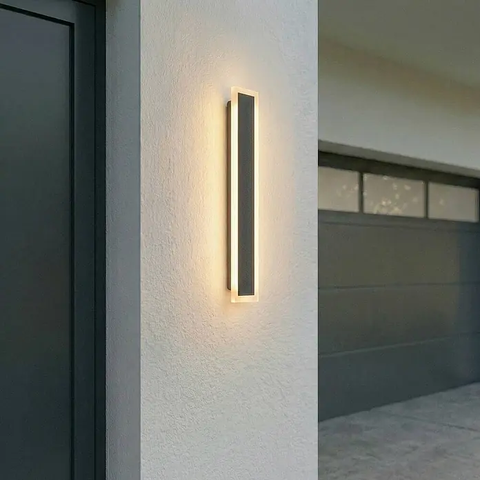 Lucande Außenwandleuchte Ilora - 3,9 x 8 x 60 cm, schwarz, schwarz, IP65 - Moderne rechteckige LED-Außenwandleuchte, dunkelgrau mit Seitenbeleuchtung, an einer strukturierten Hauswand.