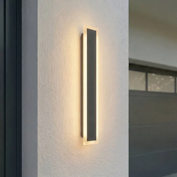 Lucande Außenwandleuchte Ilora - 3,9 x 8 x 60 cm, schwarz, schwarz, IP65 - Moderne rechteckige Outdoor-LED-Wandleuchte mit dunkelgrauem Paneel, wirft warmes Licht auf eine strukturierte Wand.
