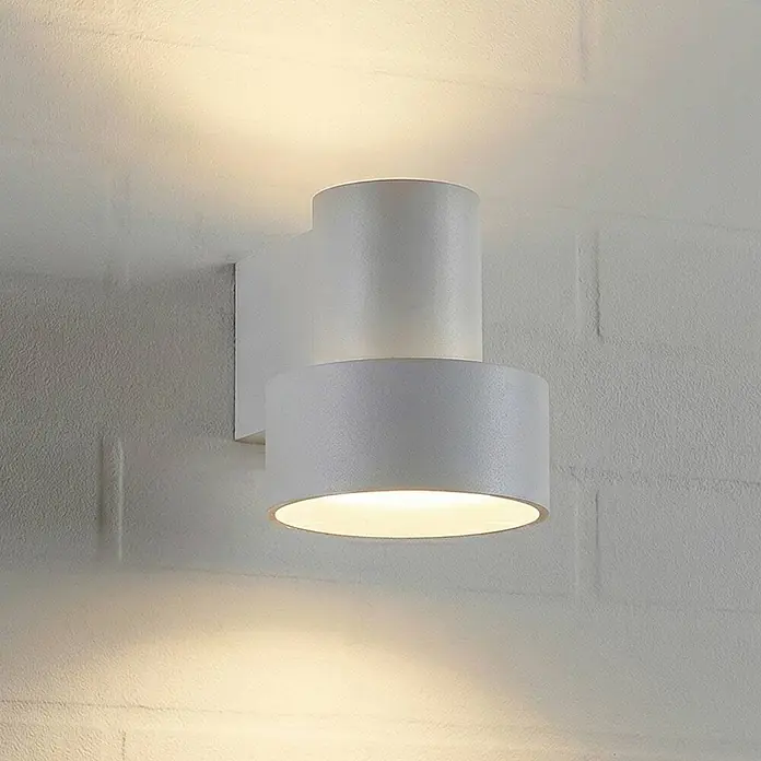 Lucande Außenwandleuchte Elune - alu / grau / zink, IP44 - Weiße zylindrische Wandleuchte an der Wand, die warmes Licht nach oben und unten abgibt.